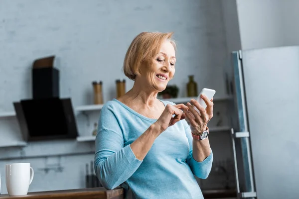 Mutfakta Smartphone Kullanarak Gülümseyen Kadın Kıdemli — Stok fotoğraf