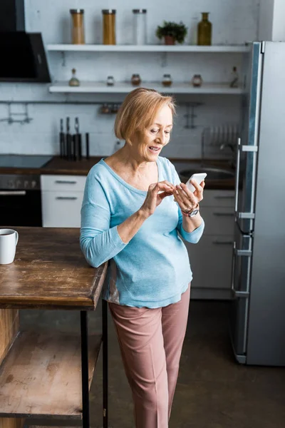 Χαμογελώντας Ανώτερων Γυναίκα Χρησιμοποιώντας Smartphone Στην Κουζίνα — Φωτογραφία Αρχείου