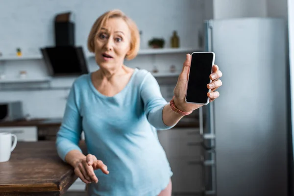 Senior Kvinna Tittar Kameran Och Presentera Smartphone Med Blank Skärm — Stockfoto