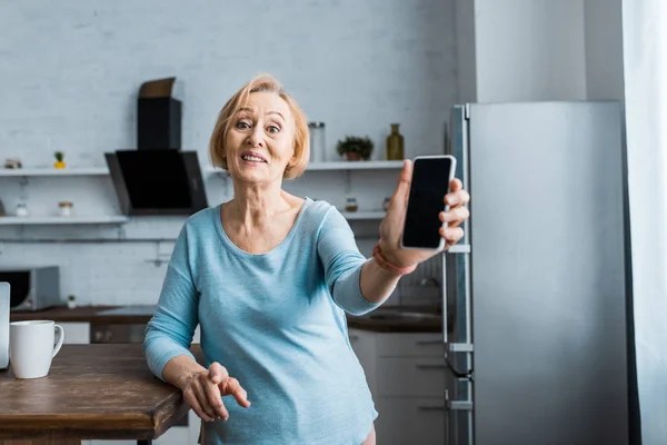 Lächelnde Seniorin Blickt Kamera Und Präsentiert Smartphone Mit Leerem Bildschirm — Stockfoto