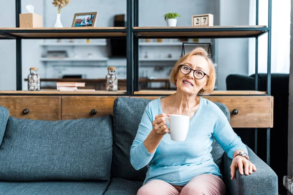 Senior Kobietę Okularach Patrząc Kamery Siedzi Kanapie Kubkiem Kawy Salonie — Zdjęcie stockowe