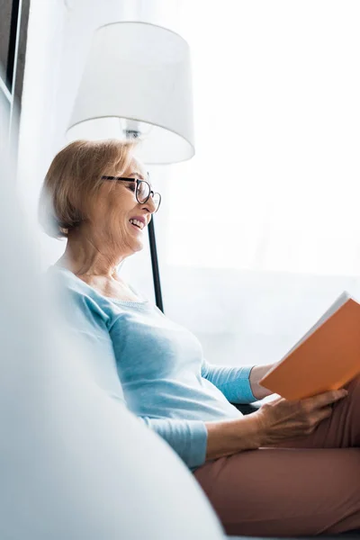 Enfoque Selectivo Mujer Mayor Sonriente Gafas Sentado Leyendo Libro Casa — Foto de Stock