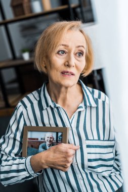 çerçeve adamla evde fotoğraf üzerinde tutan üzgün üst düzey kadın