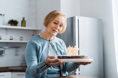'80' işareti ile pasta üstüne doğum günü kutlaması sırasında tutan yalnız üst düzey kadın