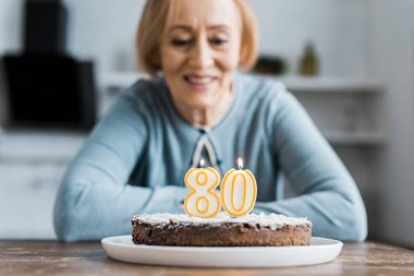 masada oturan ve pastalara '80' işareti ile üstte evde doğum günü kutlaması sırasında seyir gülümseyen kadın kıdemli