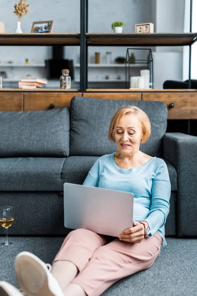 senior woman in casual clothes using laptop in living room