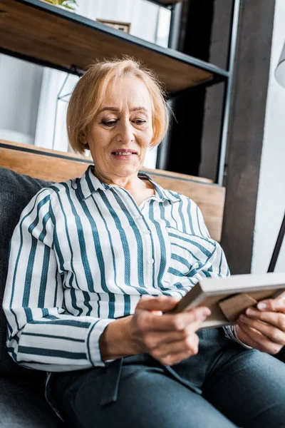 Seniorin Legerer Kleidung Sitzt Und Schaut Auf Bilderrahmen — Stockfoto