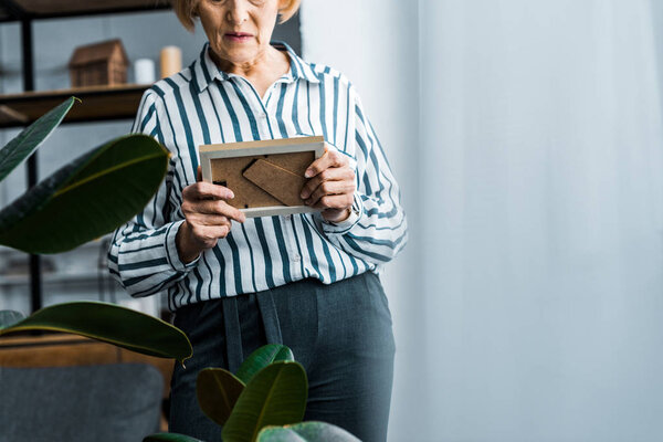 обрезанный вид пожилой женщины, смотрящей на рамку дома с копировальным пространством
