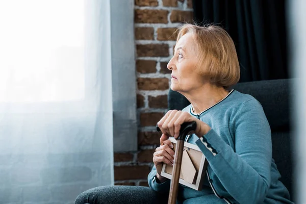 Verärgerte Seniorin Sitzt Mit Gehstock Und Hält Bilderrahmen Hause — Stockfoto