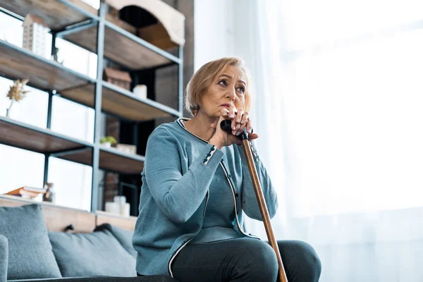 ソファに座って コピー領域を持つ家庭で杖を保持している悲しい年配の女性 — ストック写真