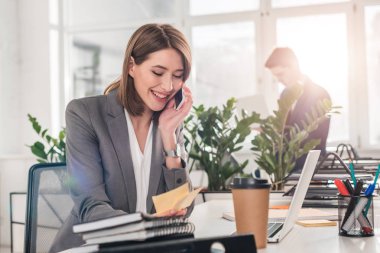 seçici odak neşeli işkadını arka plan üzerinde iş arkadaşınız ile smartphone üzerinde konuşurken yapışkan notlar arıyorum