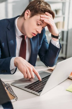 handsome tired businessman sitting near laptop in office  clipart