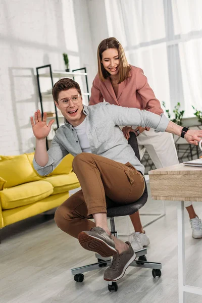 Cheerful Woman Smiling While Pushing Chair Scared Boyfriend — Stock Photo, Image