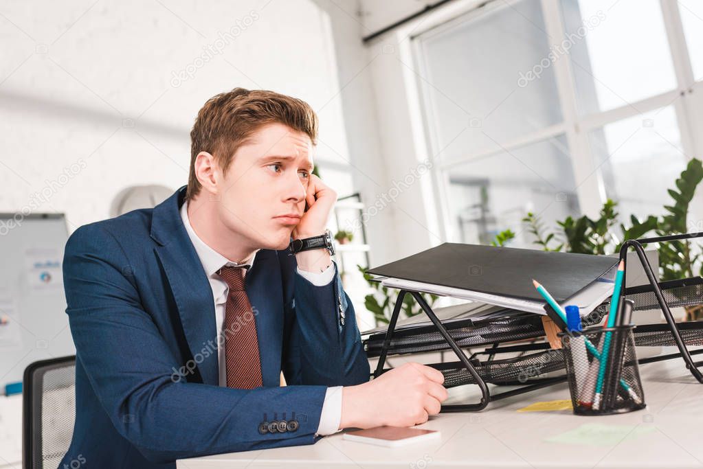 bored businessman sitting near document tray in office 