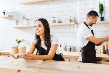 sayaç arkasında duran ve kağıt bardak wile barista kahve evde çalışma tutan çekici esmer kasiyer