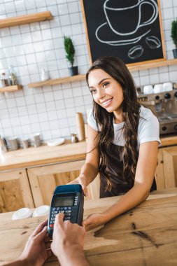 yakınındaki bar counter kahverengi önlük ayakta ve kahve evin içinde işlem yapma terminal wile adam tutarak çekici kasiyer