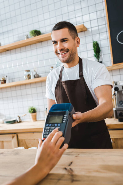 handsome cashier standing near bar counter and holding terminal wile woman making transaction in coffee house