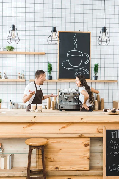 cashiers standing behind bar counter, talking and smiling in coffee house