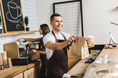 yakışıklı kasiyer veren kağıt bardak ve çanta barista kahve evde sayaç bar arkasında kahve yapma cezbetmek