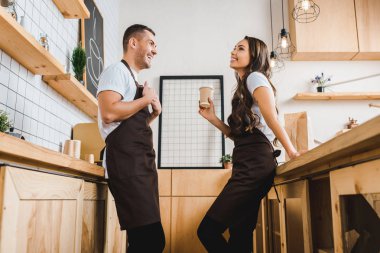 kağıt bardak tutan ve barista ahşap bar counter coffee House yakınındaki kahverengi önlük ile konuşurken kasiyer