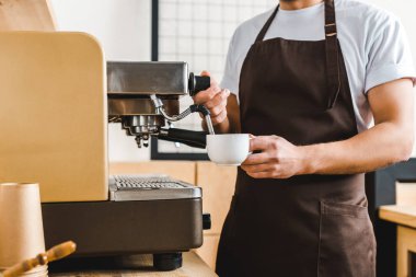 kırpılan Kupası tutarak ve kahve makinesi kahve evin içinde yakışıklı barista görünümünü