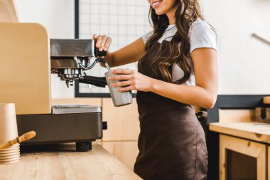 kırpılan Kupası tutarak ve kahve makinesi kahve evin içinde çekici esmer barista görünümünü