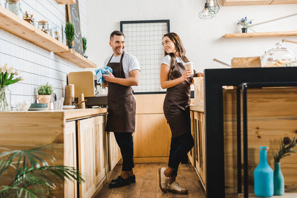 barista and cashier standing behind bar counter in coffee house