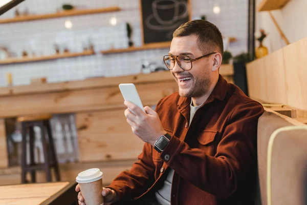 Kjekken Mann Burgunder Skjorte Sitter Sofaen Holder Papirkopp Ser Smarttelefonen – stockfoto