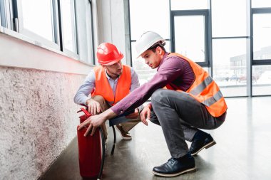 handsome firemen in helmets checking red extinguishers  clipart