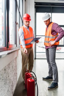 firemen in helmets standing and looking at red extinguishers  clipart