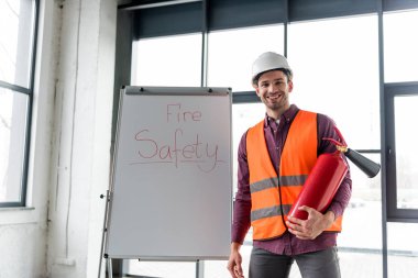 mutlu itfaiyeci yangın emniyet yazı ile beyaz tahta yakın duran kırmızı söndürücü holding