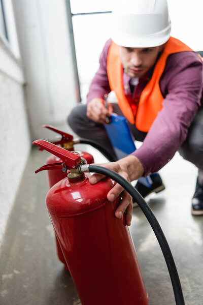 selective focus of red extinguishers near fireman with clipboard in hand