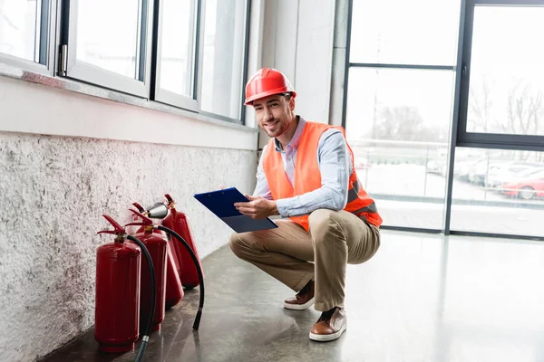 Happy Fireman Helmet Holding Clipboard Pen While Looking Camera Extinguishers — Stock Photo, Image