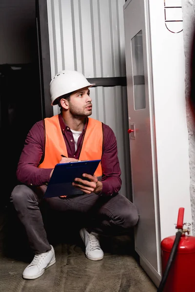 Thoughtful Firefighter Helmet Sitting Looking Fire Panel While Holding Clipboard — Stock Photo, Image