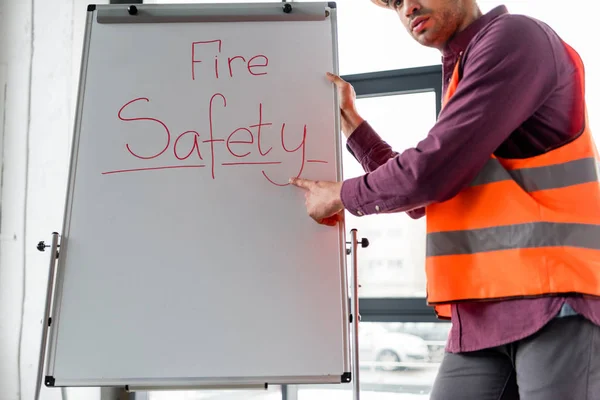 cropped view of fireman pointing with finger while standing near white board with fire safety lettering