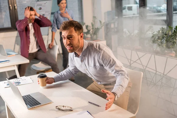 Guapo Hombre Negocios Sosteniendo Taza Papel Gritando Cerca Colegas Oficina —  Fotos de Stock