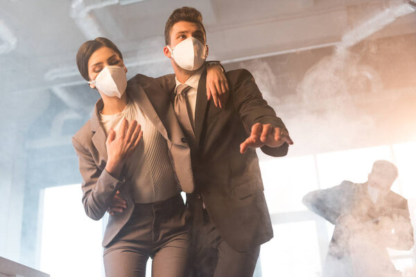 selective focus of terrified businessman in mask standing with female coworker in office with smoke
