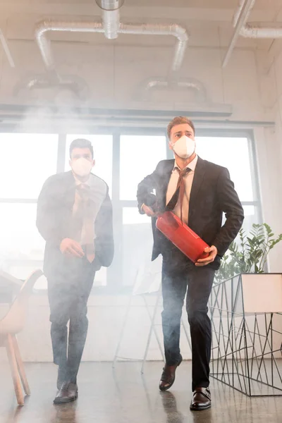 商人在办公室里带着浓烟走在同事身边 戴着口罩拿着灭火器 — 图库照片