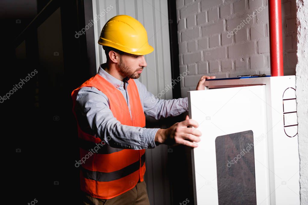 handsome fireman in helmet standing and looking at fire panel 