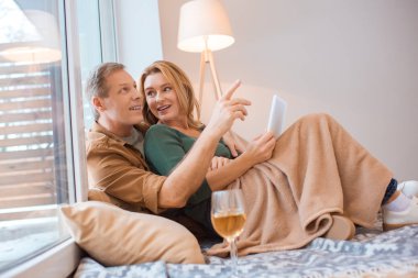 smiling man pointing with finger while using digital tablet together with wife clipart