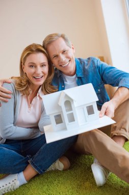happy couple demonstrating house model while looking at camera clipart