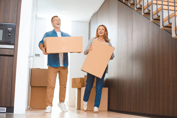 smiling couple holding cardboard boxes at new home