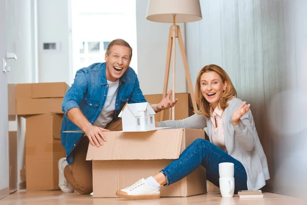 Pareja Feliz Emocionada Mostrando Modelo Casa Mientras Desempaca Caja Cartón — Foto de Stock