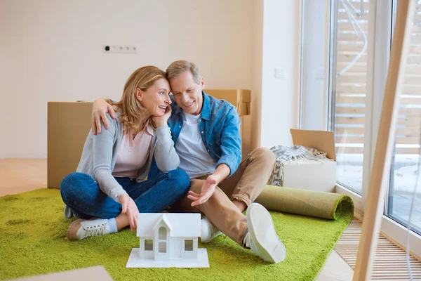 Feliz Pareja Abrazándose Mientras Está Sentado Alfombra Verde Cerca Modelo — Foto de Stock