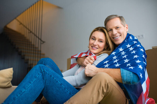 happy couple wrapping in usa national flag and looking at camera