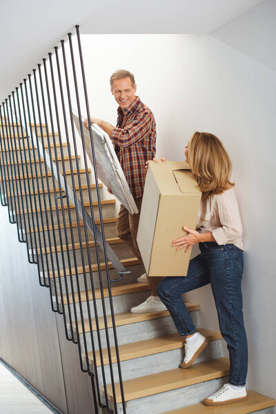 woman with cardboard box and man with picture going upstairs