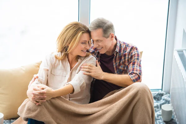 幸福的丈夫拥抱微笑的妻子 而坐在羊毛毯子下的窗口 — 图库照片