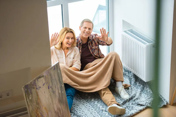 Pasangan Bahagia Melambaikan Tangan Sambil Duduk Lantai Dengan Jendela Besar — Stok Foto