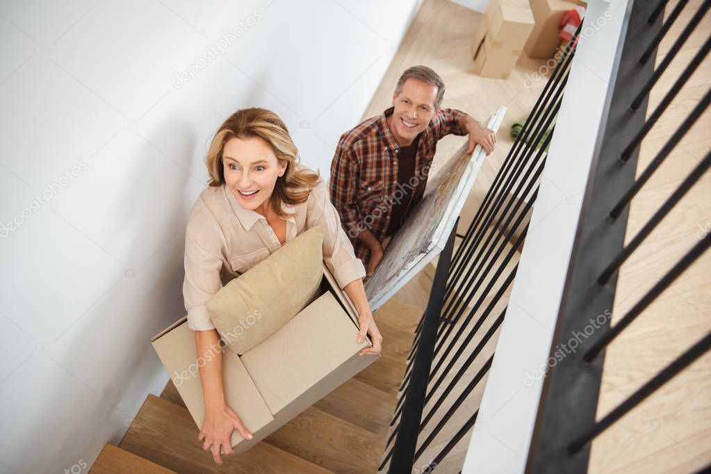 woman with carton box and man with picture going upstairs at new home