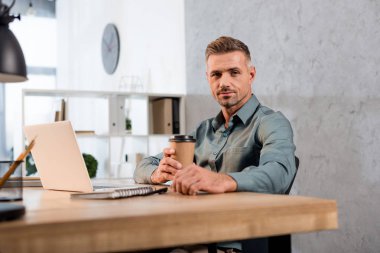yakışıklı işadamı kamera dizüstü Office yakınındaki bakarken kağıt bardak tutan